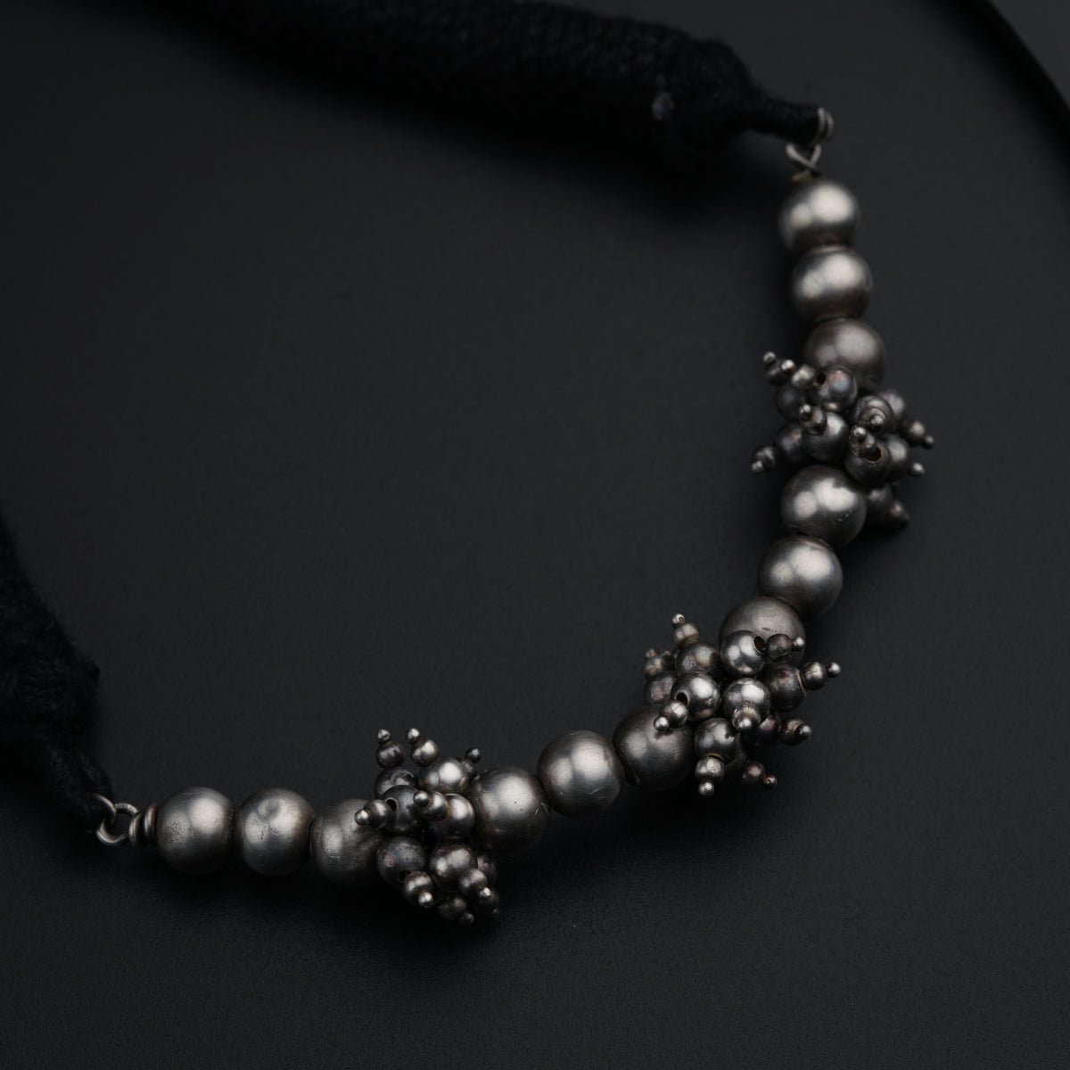 a black necklace with silver beads on a black surface
