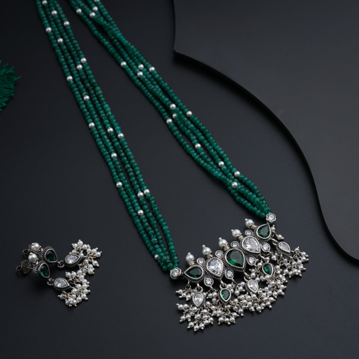 a green necklace and matching earrings on a black surface