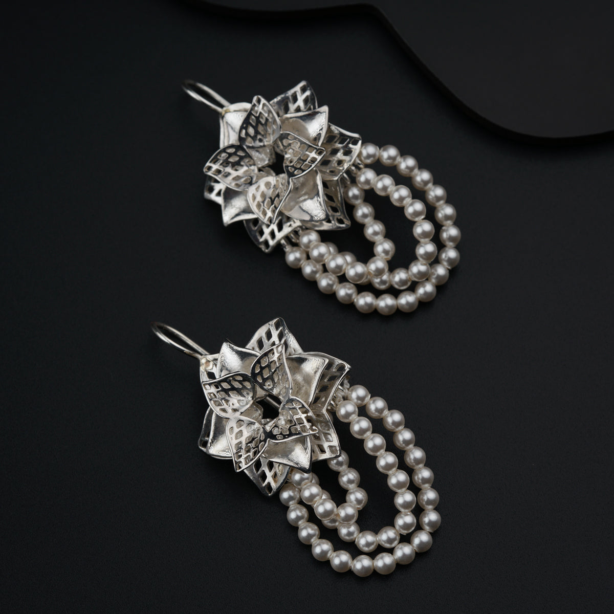 a pair of earrings with pearls on a black surface