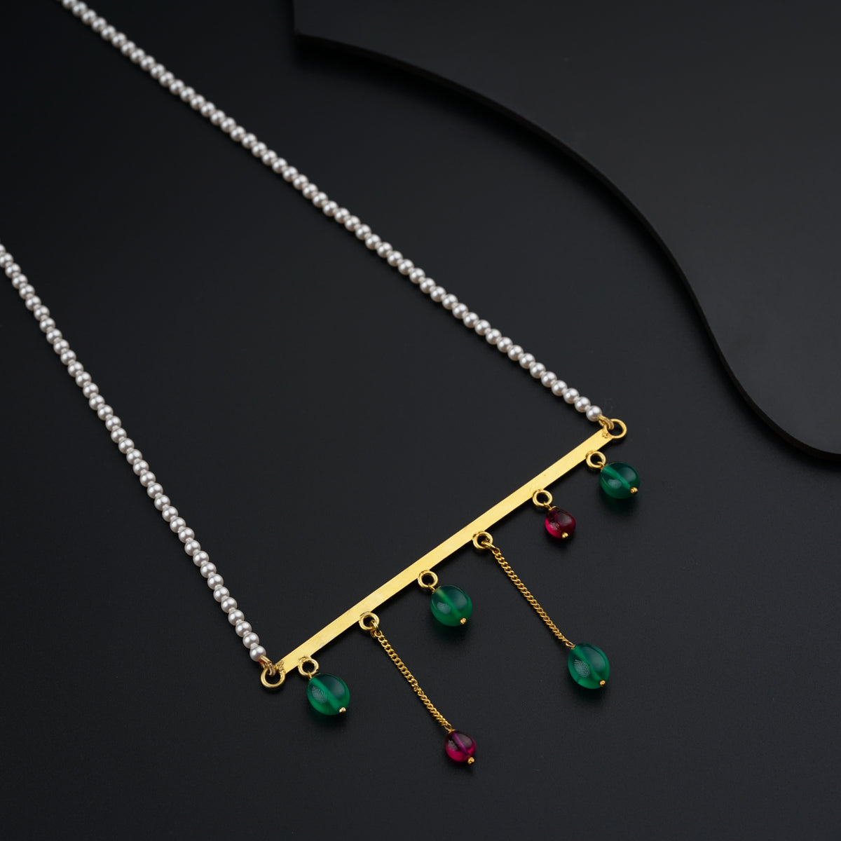 a gold necklace with green and red beads on a black surface