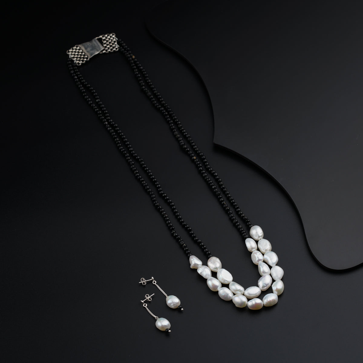 a necklace and earring with pearls on a black surface