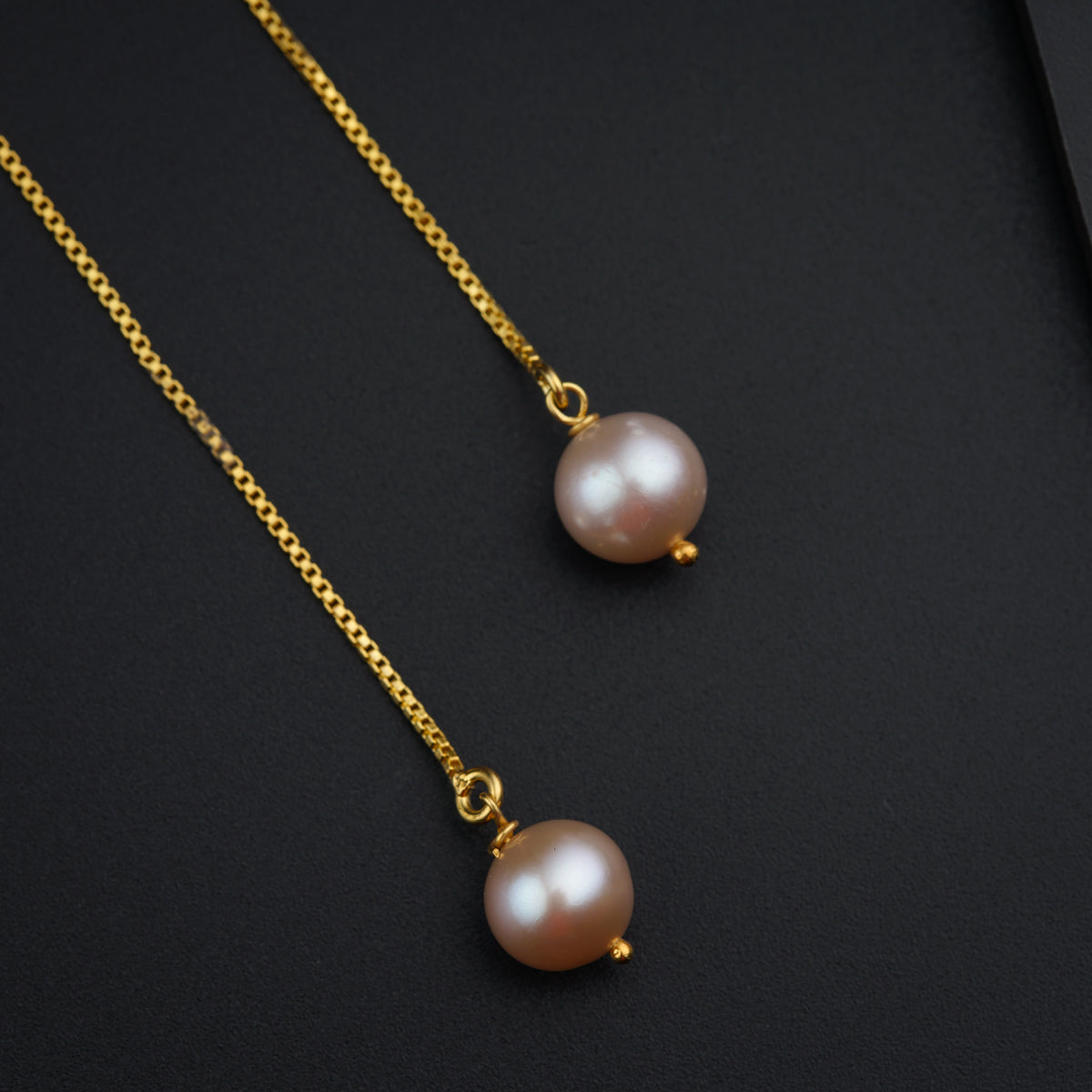 a pair of pearl necklaces on a black surface