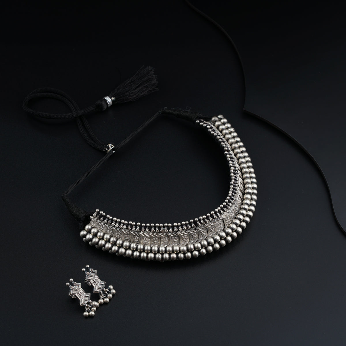 a necklace and earring with a tassel on a black background