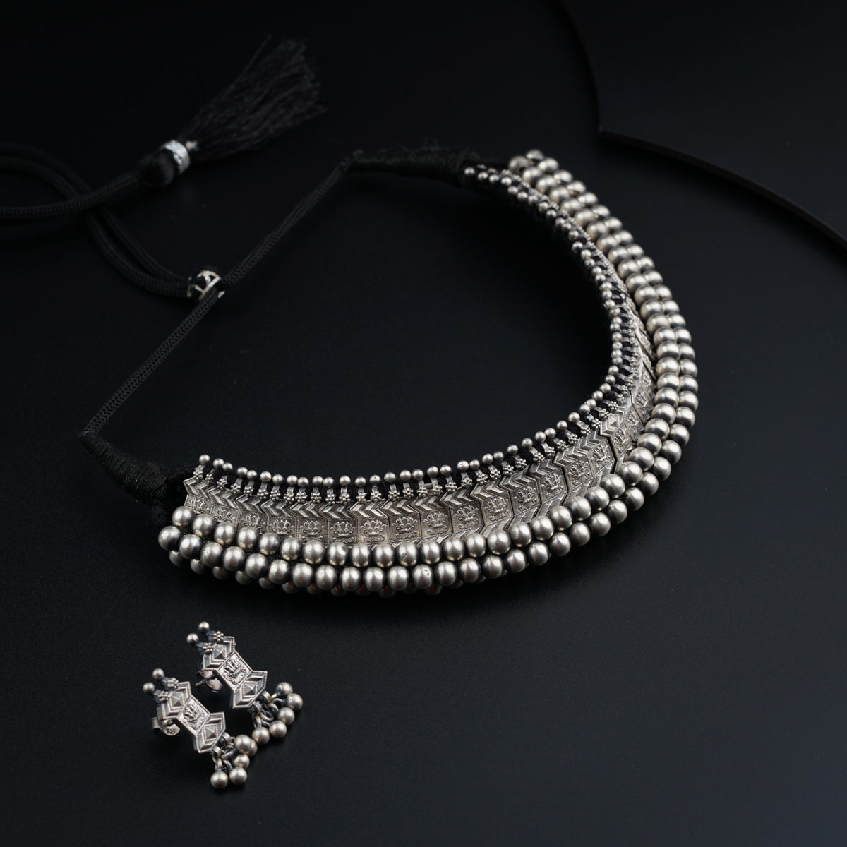 a silver necklace with a cross charm on a black background