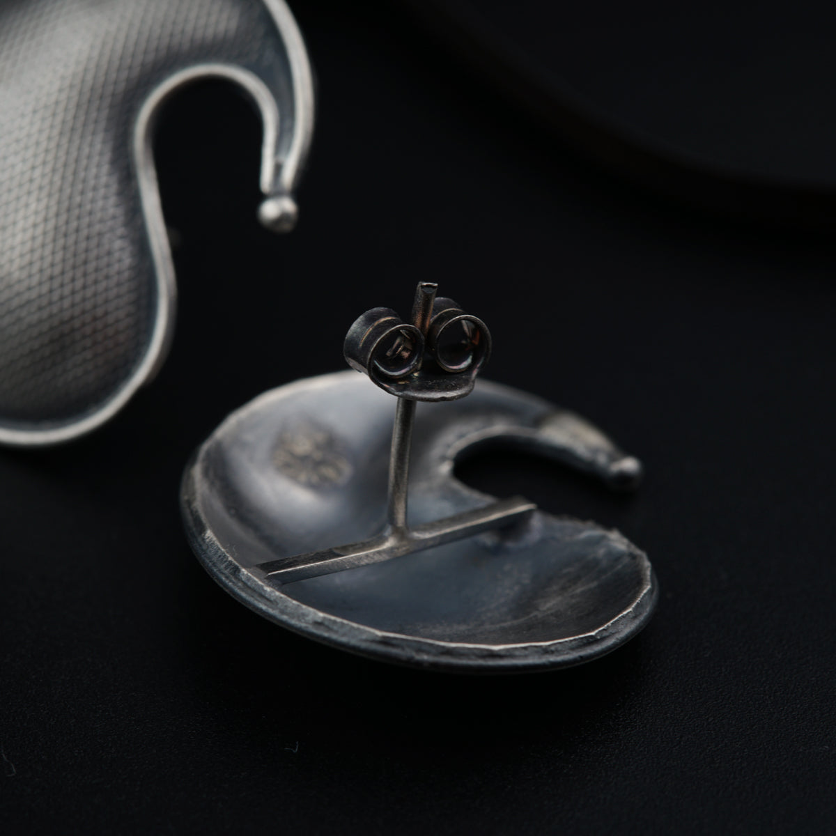 a pair of silver ear clips sitting on top of a black surface