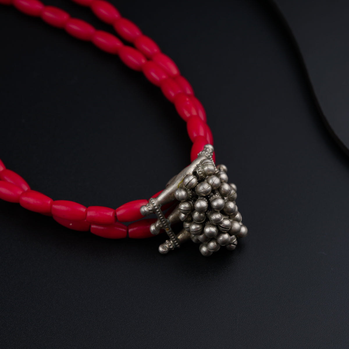 a red necklace with silver beads on a black surface
