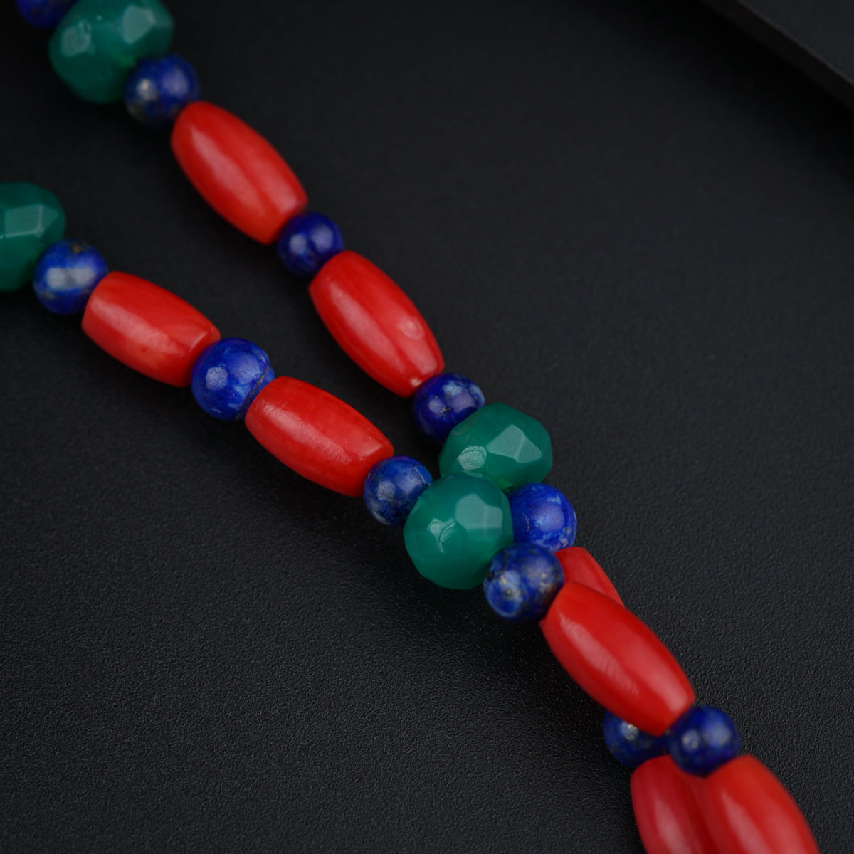 a red, blue, and green beaded necklace on a black surface