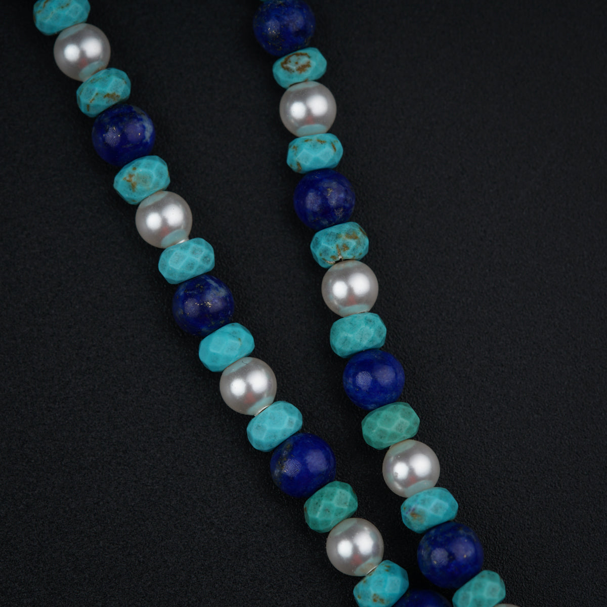 a necklace with pearls and blue beads on a black surface