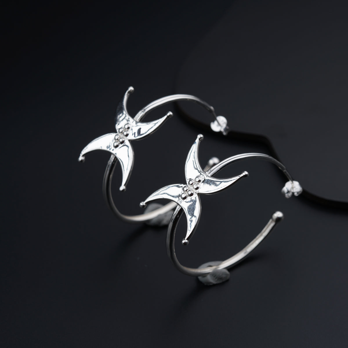 a pair of silver earrings on a black surface