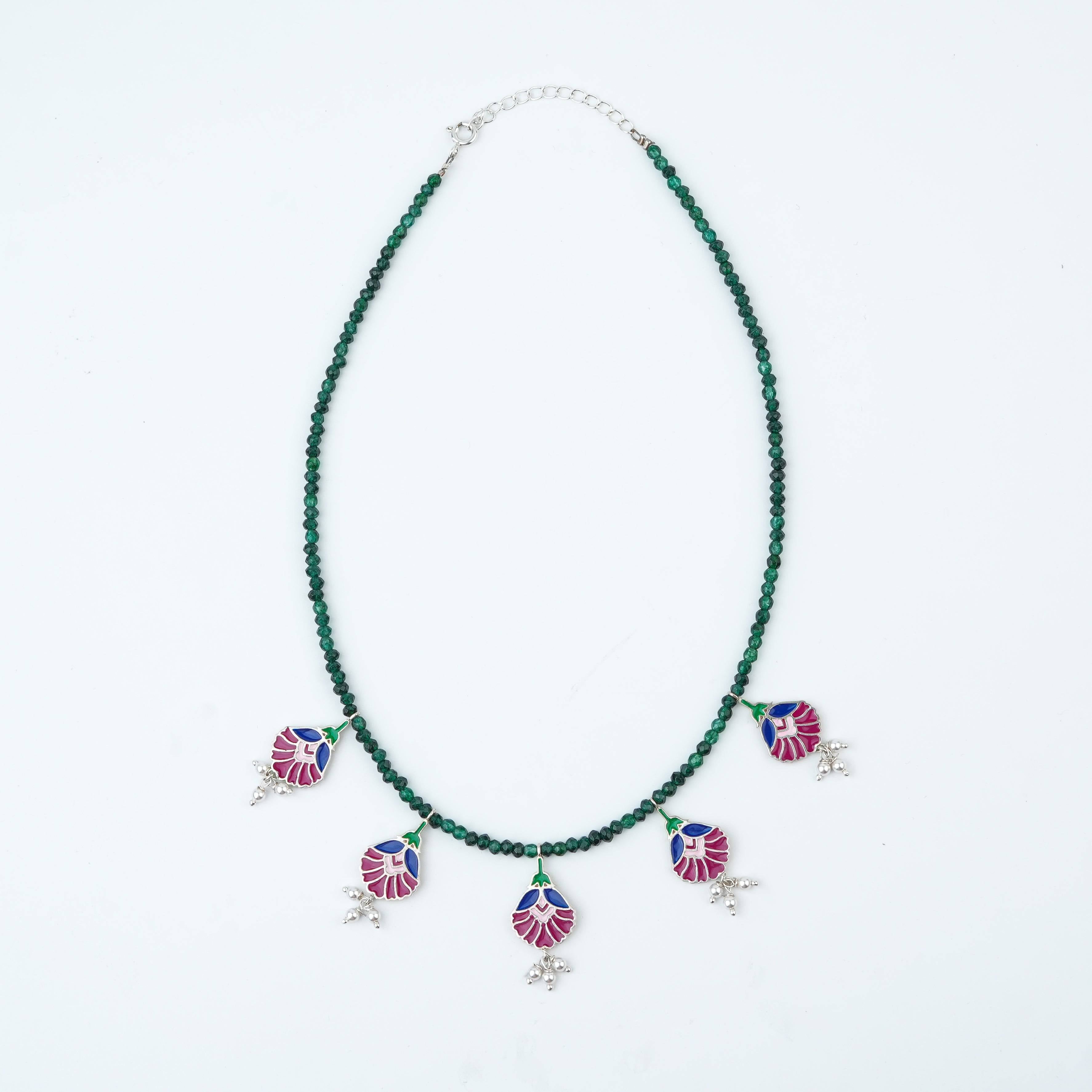Flat-lay of Rose Enamel Flower Charm Necklace with Green Onyx with floral accessories and complementary silver jewellery