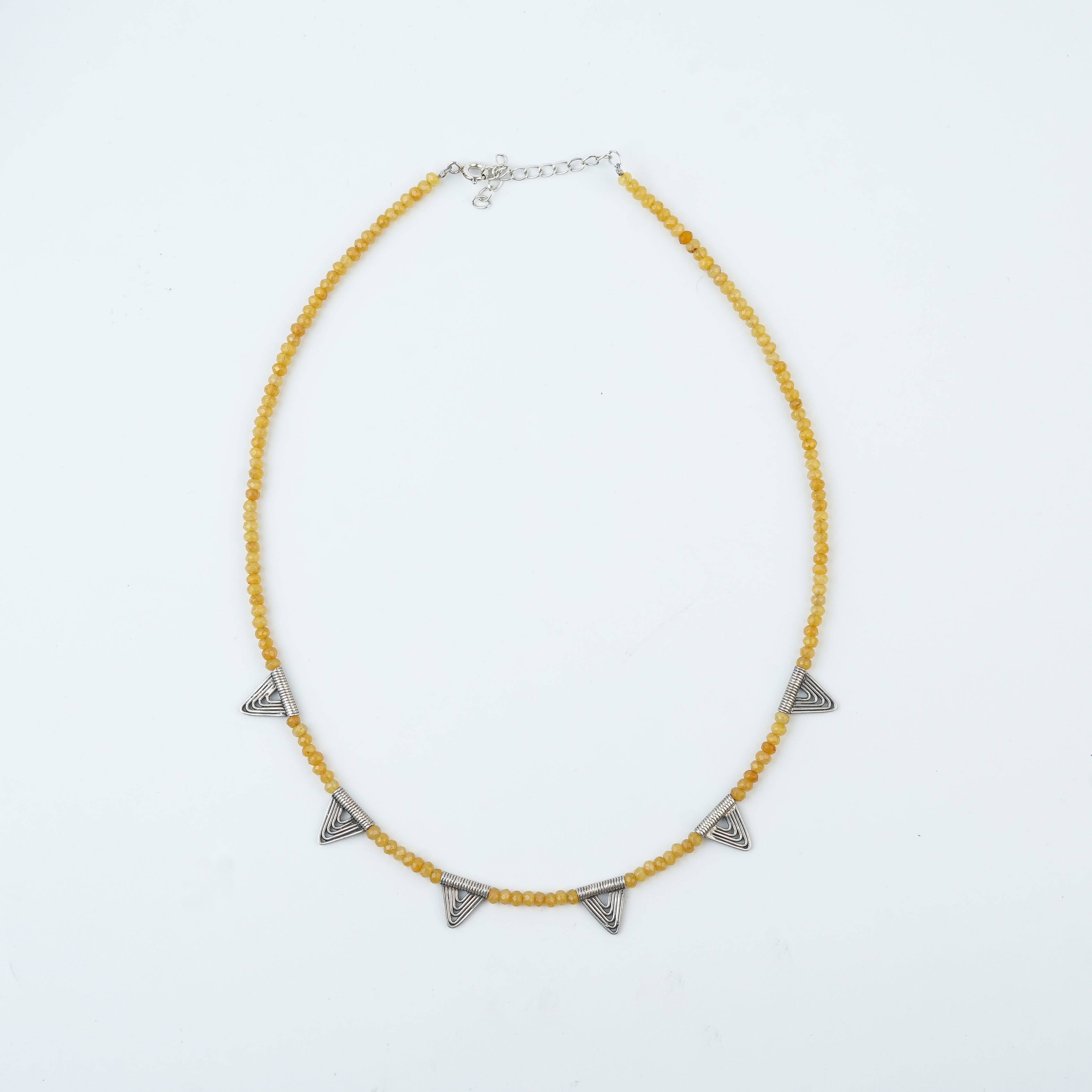 Flat-lay of a triangle charm necklace with Yellow Jade with complementary jewellery and elegant styling accessories