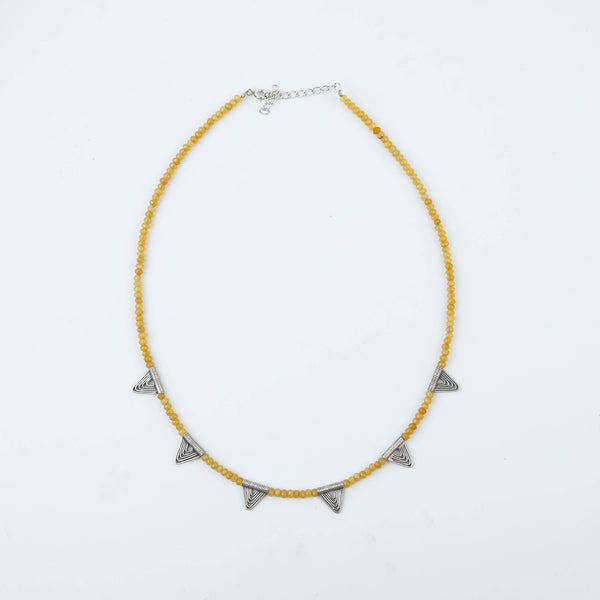 Flat-lay of a triangle charm necklace with Yellow Jade with complementary jewellery and elegant styling accessories