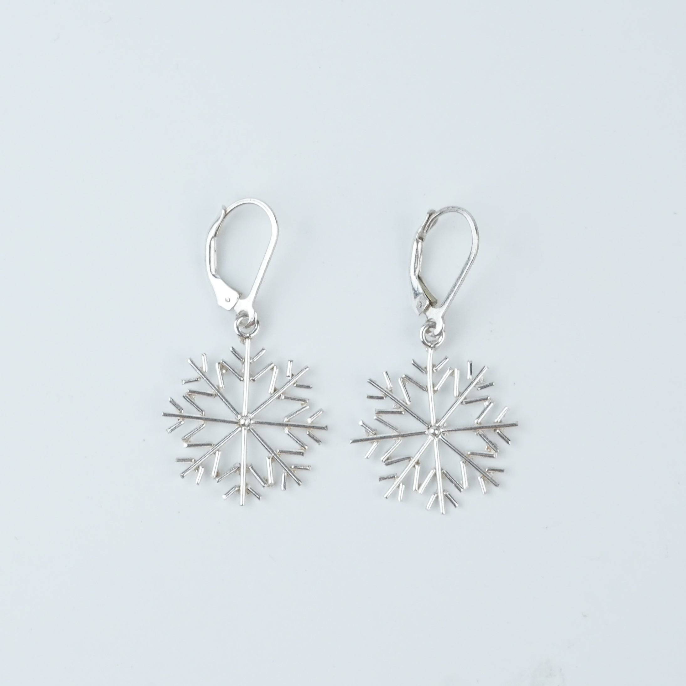 Flat-lay of Silver Snowflake Dangle Earrings with complementary jewellery and elegant styling accessories
