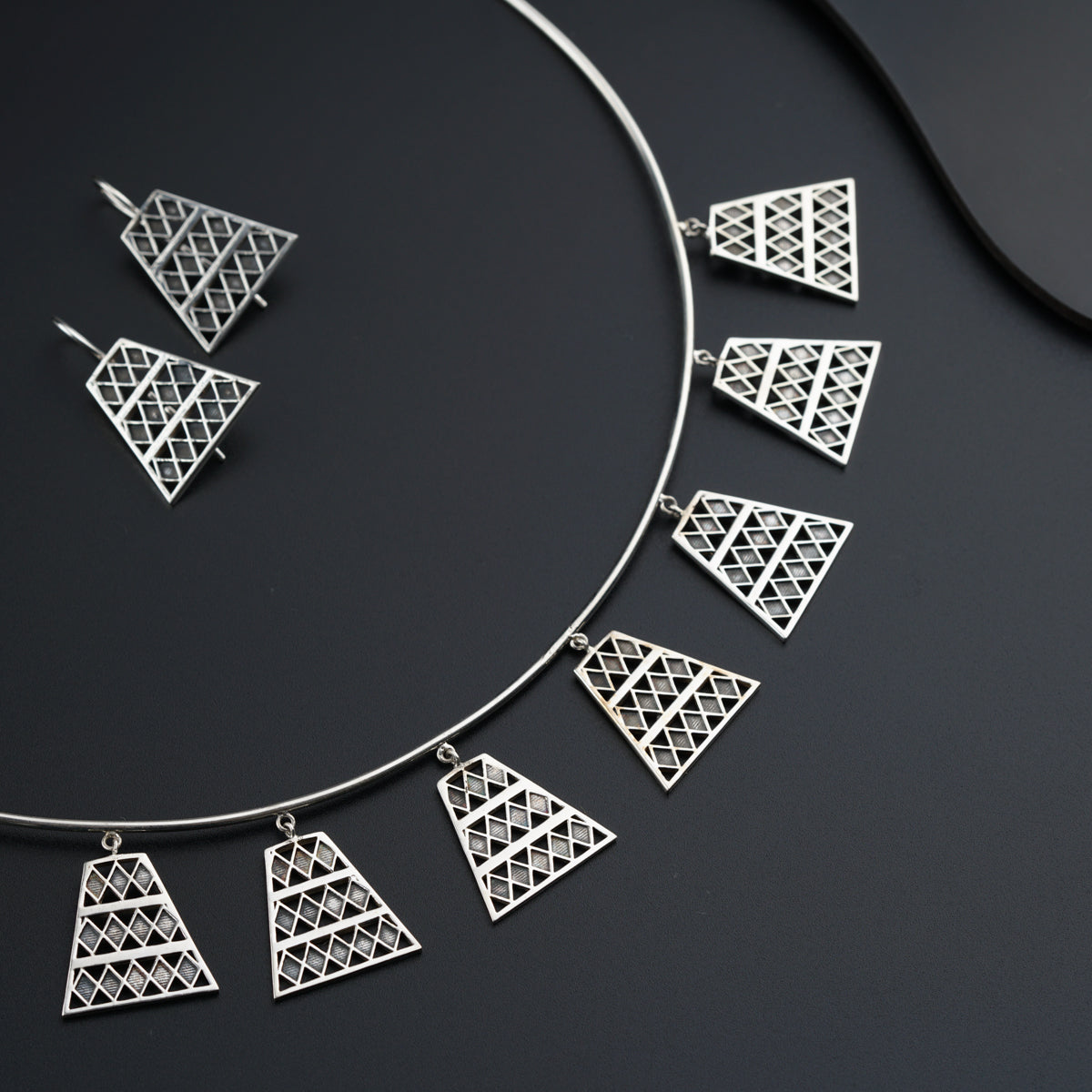 a silver necklace and matching earrings on a black surface