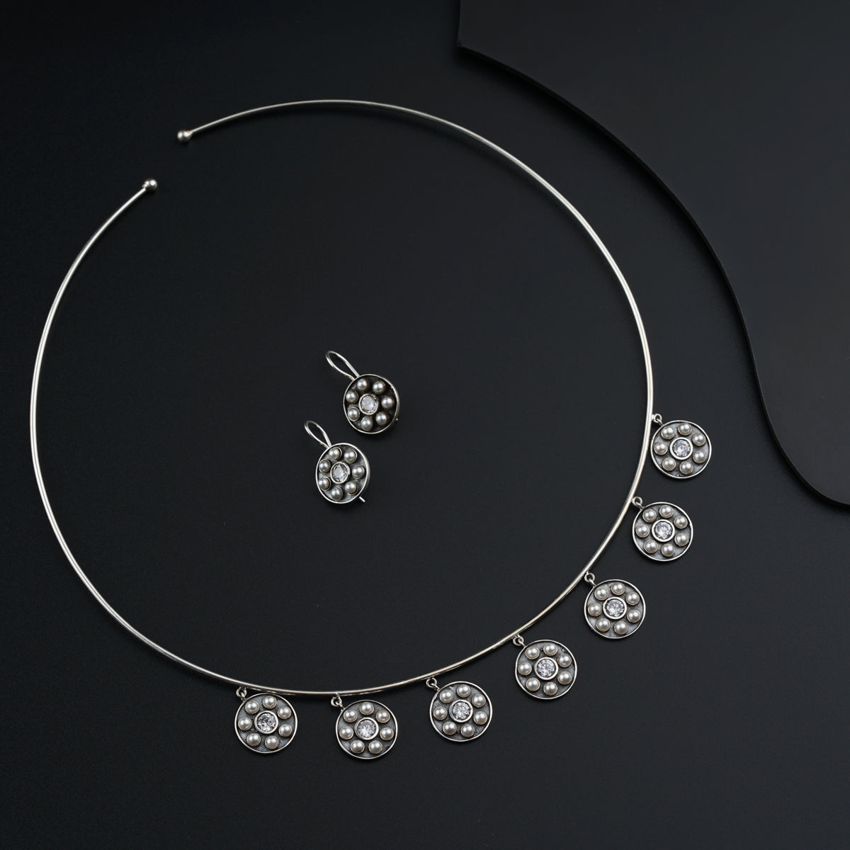 a silver necklace and earring set on a black surface