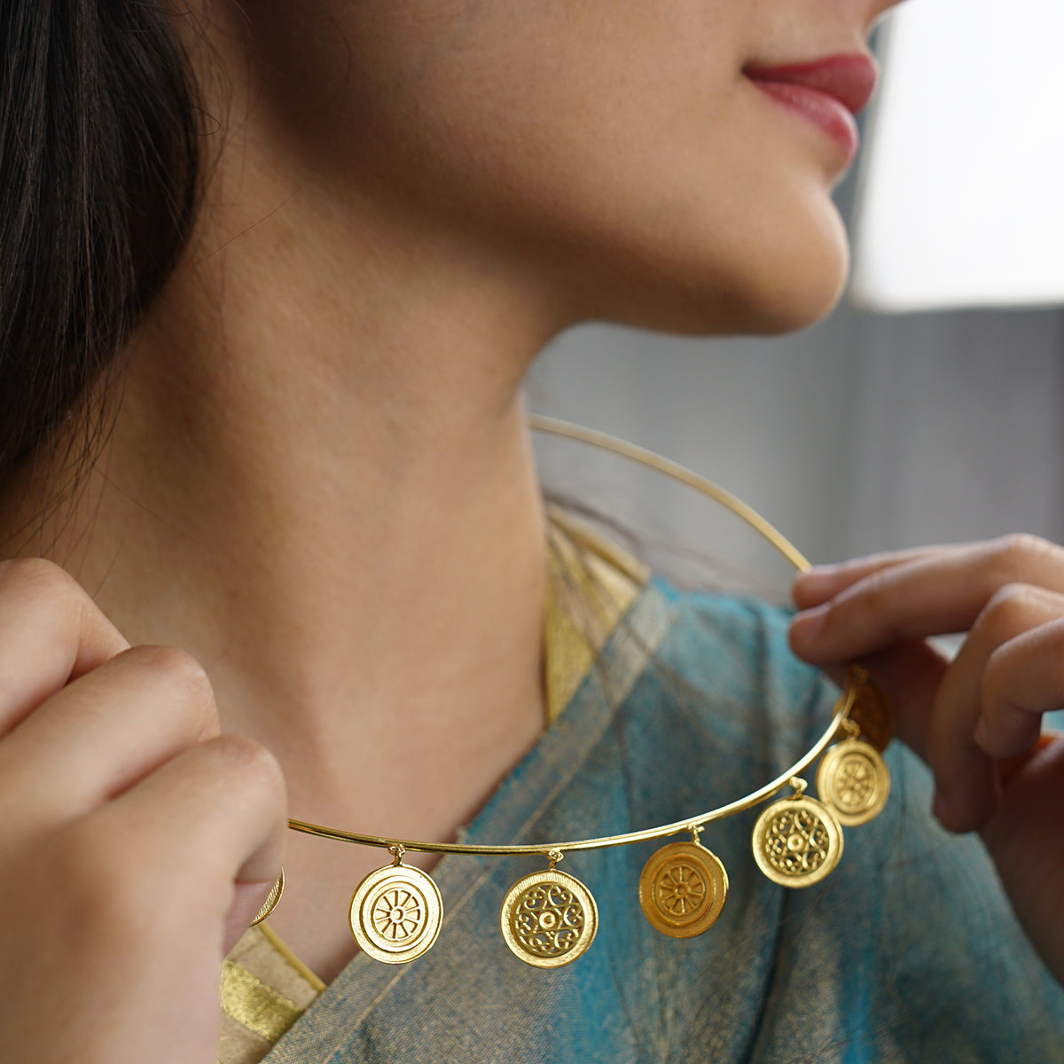a woman wearing a gold necklace with four medallions on it
