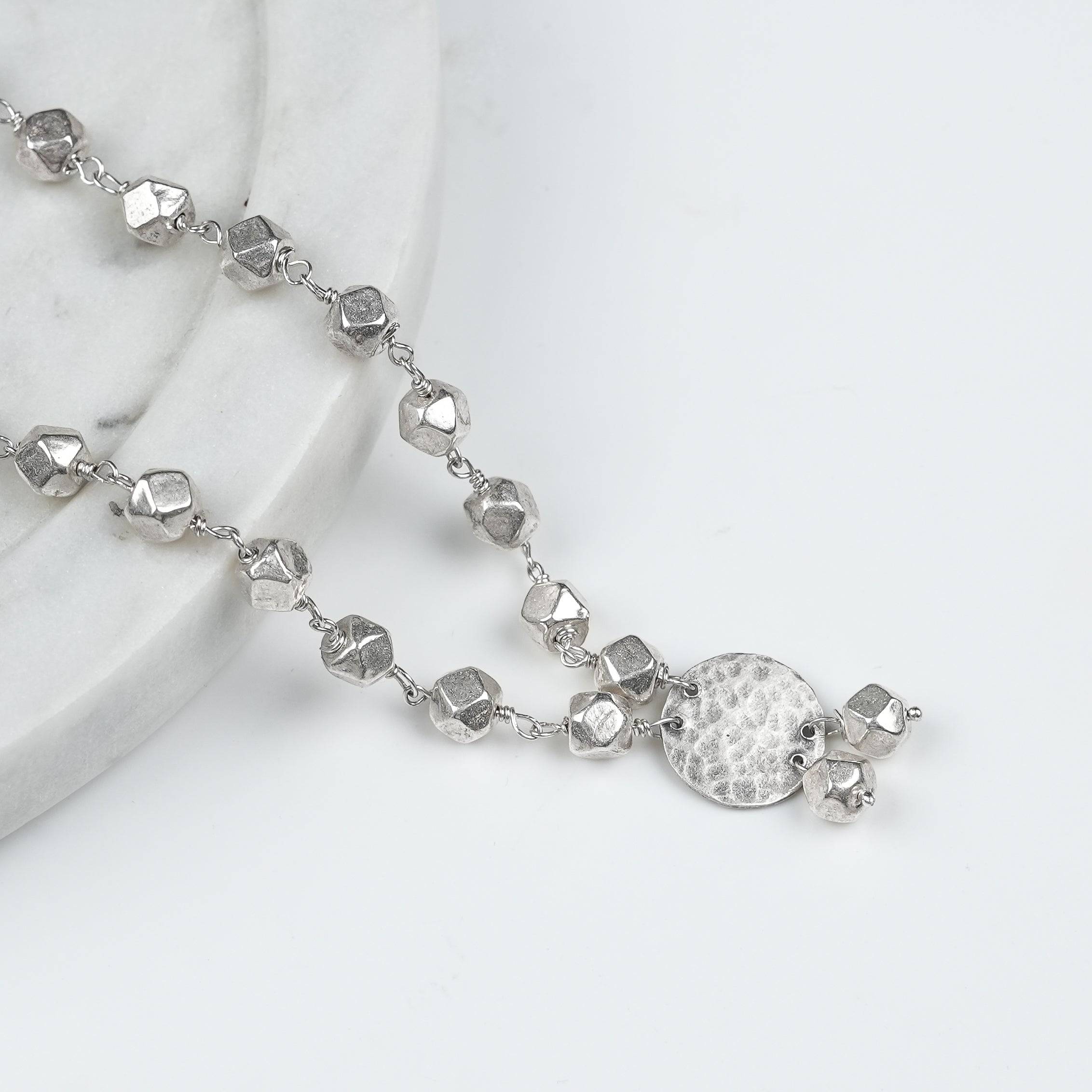 Angled view of Ashtapailu Necklace with Hammered Coin Pendant (Small) in 92.5 sterling silver with a textured coin pendant