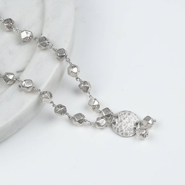 Angled view of Ashtapailu Necklace with Hammered Coin Pendant (Small) in 92.5 sterling silver with a textured coin pendant