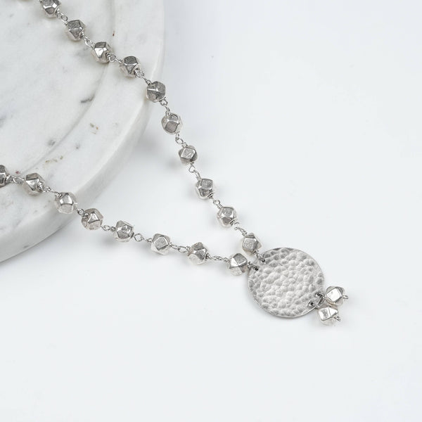 Angled view of Ashtapailu Necklace with Hammered Coin Pendant in 92.5 sterling silver with a textured hammered coin pendant