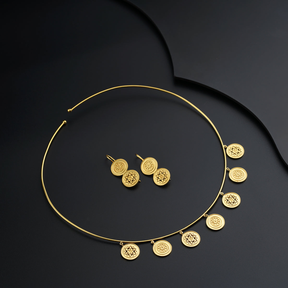 a gold necklace and earring set on a black surface