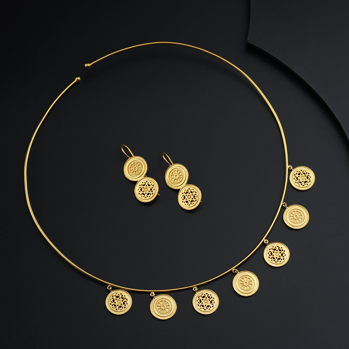 a gold necklace and earring set on a black surface