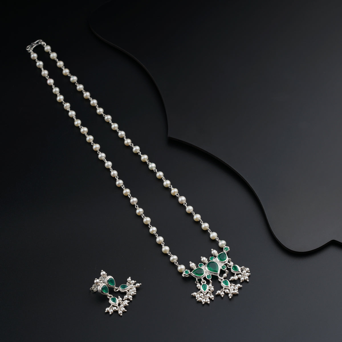 a pair of pearls and emerald necklaces on a black surface