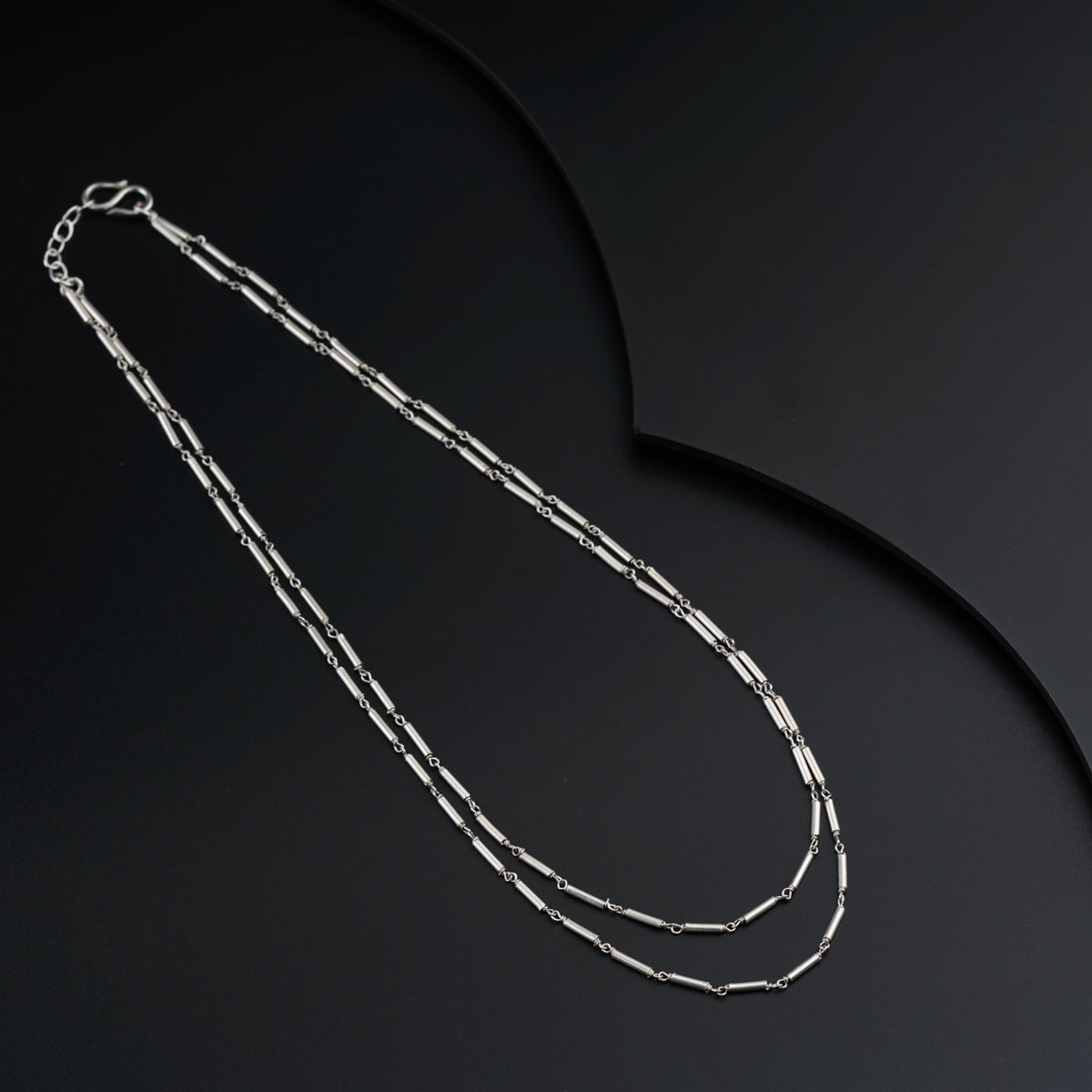 a long silver necklace with a long chain on a black background