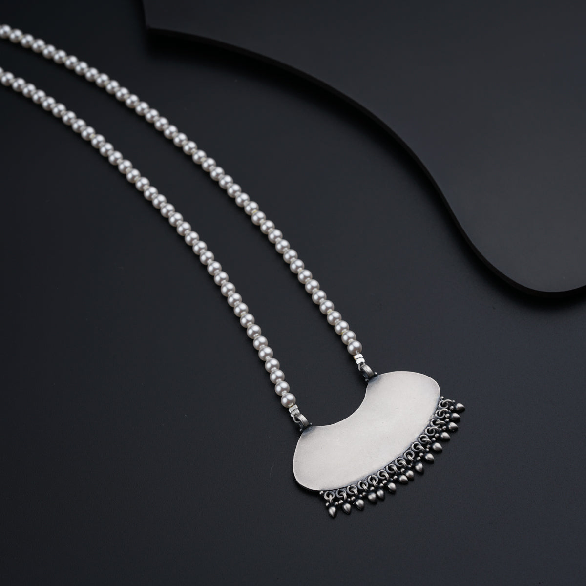 a silver necklace with a white disc on a black surface