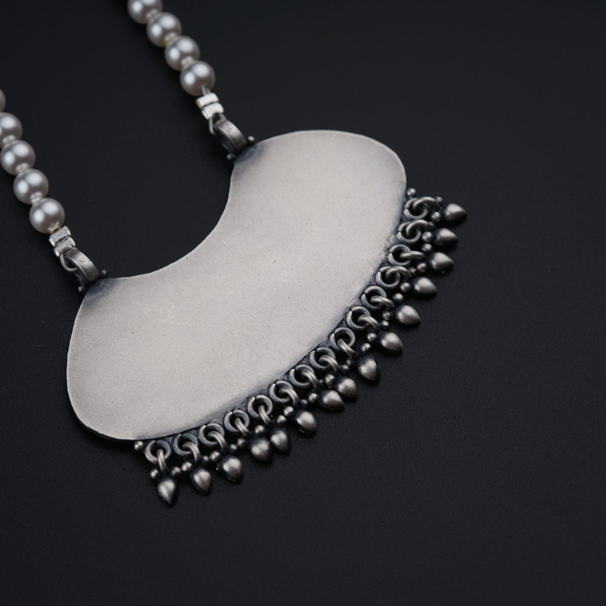 a silver necklace with pearls and beads on a black background