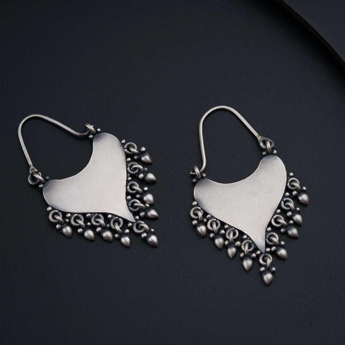 a pair of silver toned earrings on a black surface