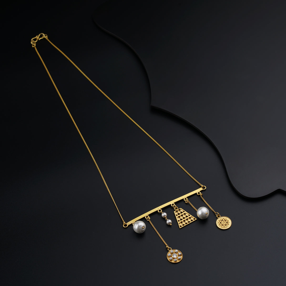 a gold necklace with pearls and charms on a black background