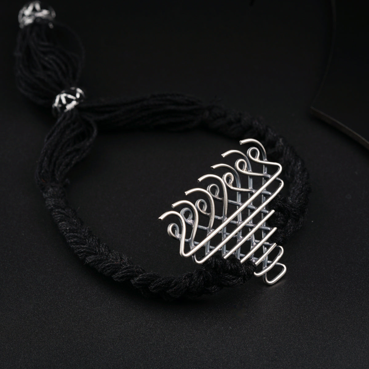 a black string bracelet with a silver pendant