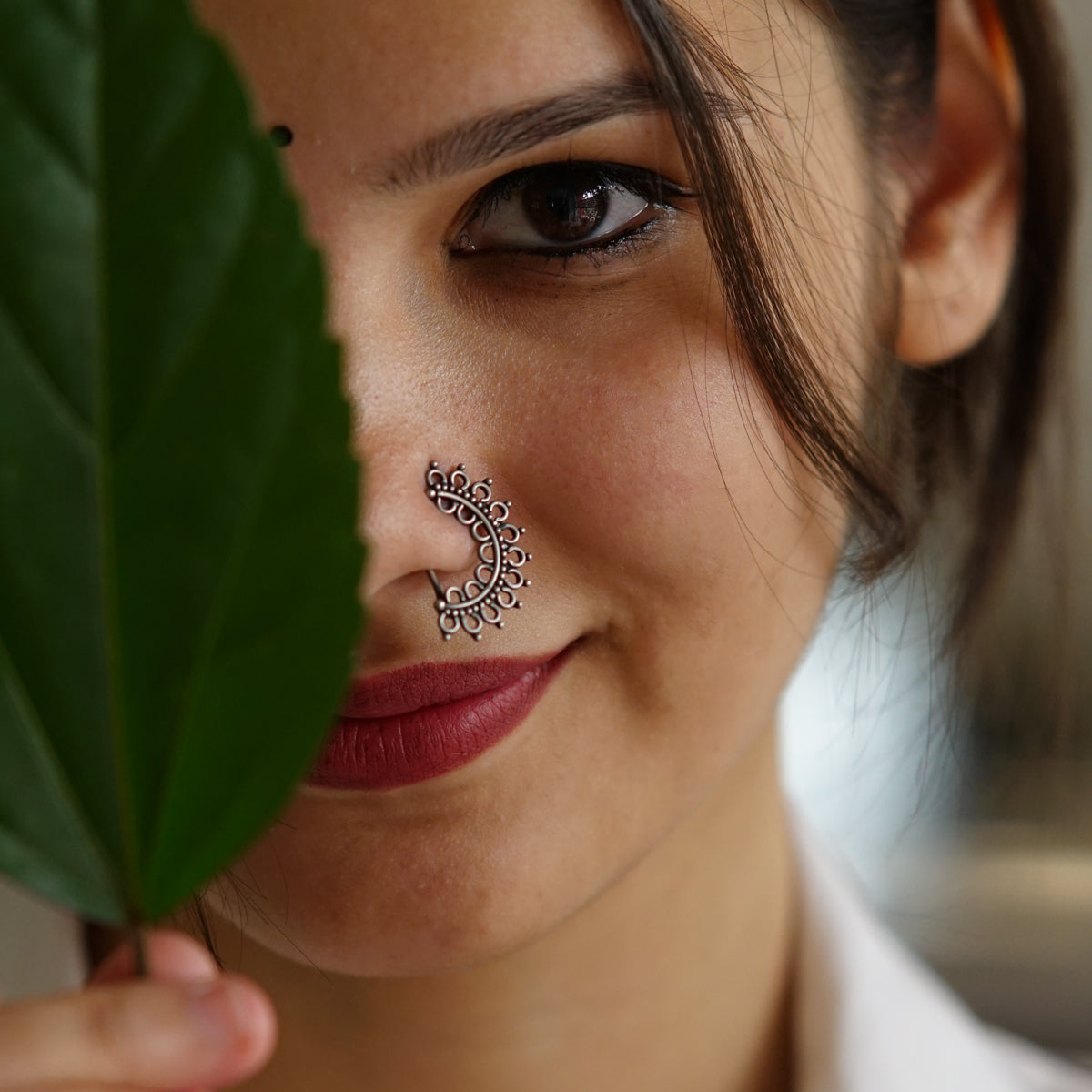 a woman holding a leaf with a nose piercing on it