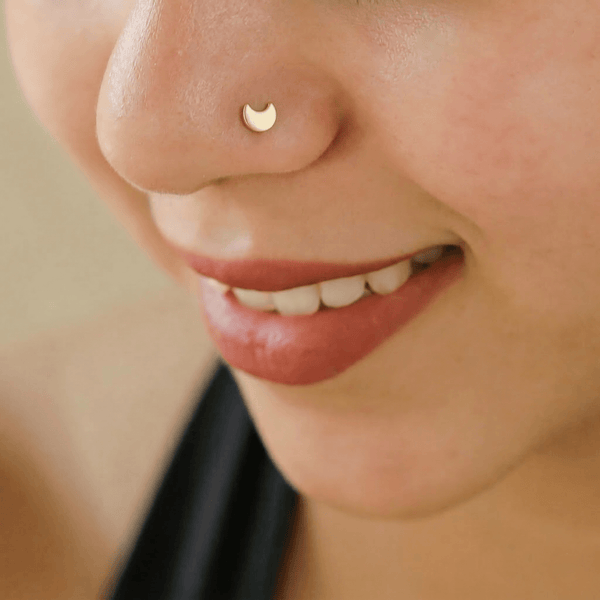 Pierced gold-plated crescent moon nose pin on white background
