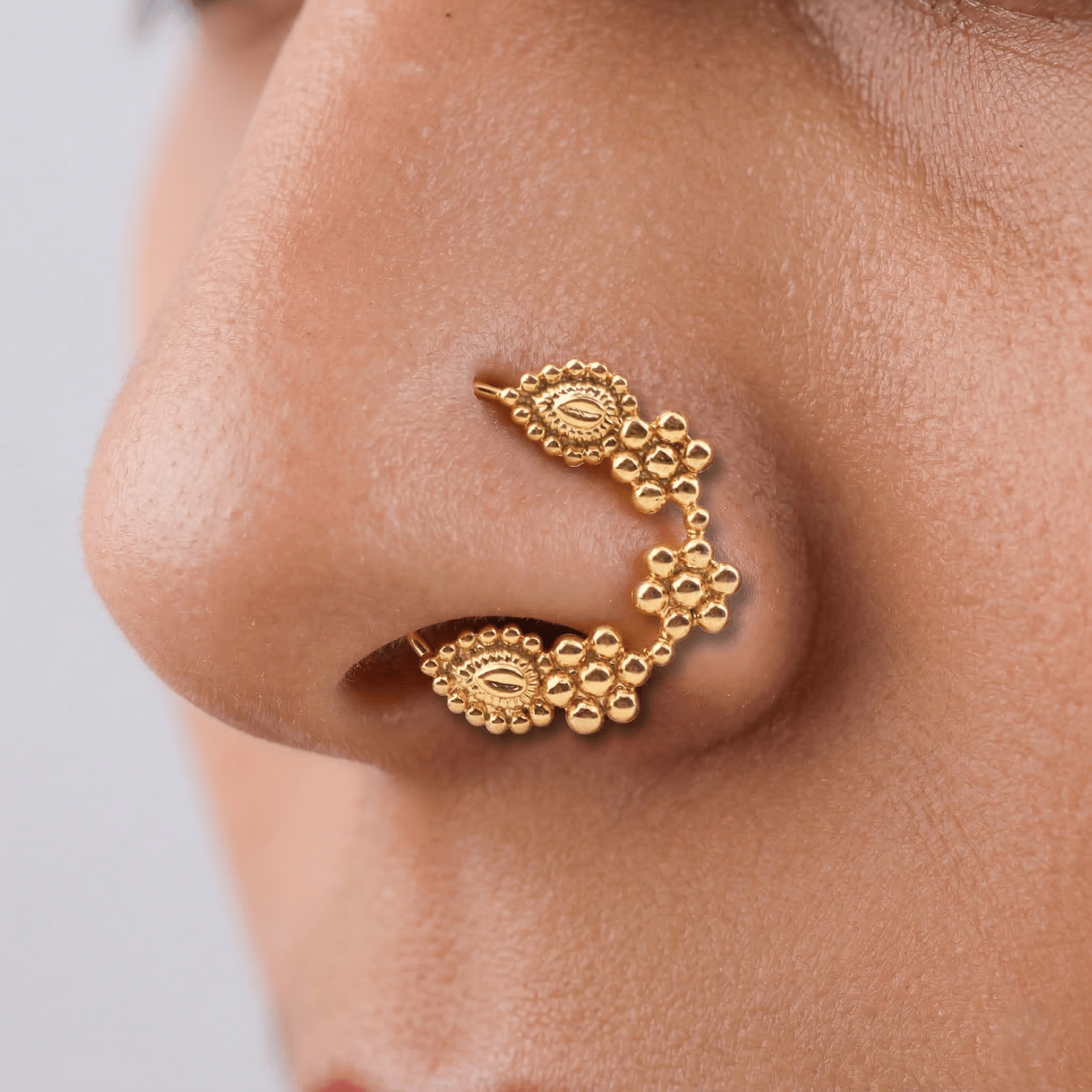 Close-up of gold nose ring on skin showing detailed craftsmanship