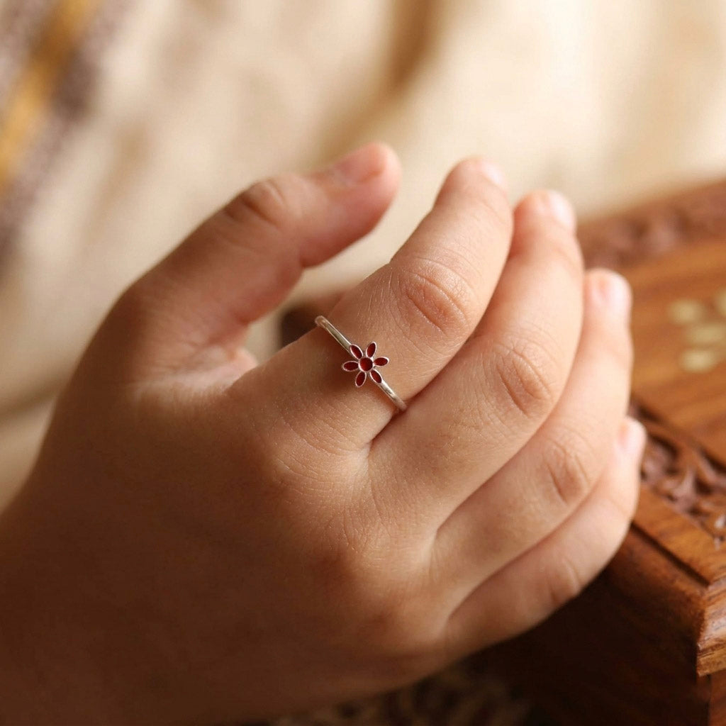 Close-up of red enamel flower ring worn on finger