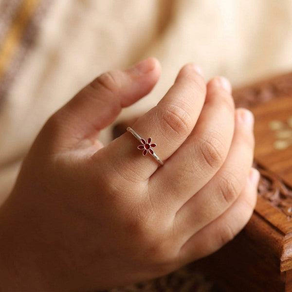 Close-up of red enamel flower ring worn on finger