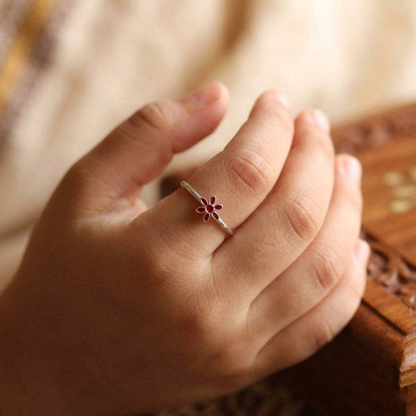 Close-up of red enamel flower ring worn on finger
