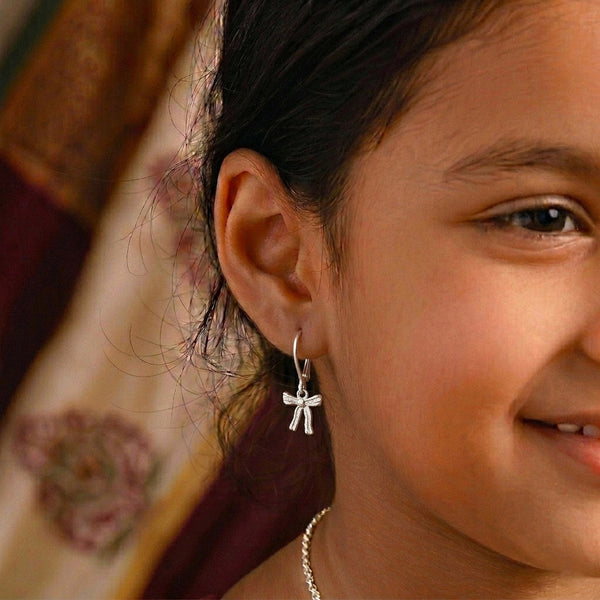 Close-up of a woman's ear with silver bow dangle earrings