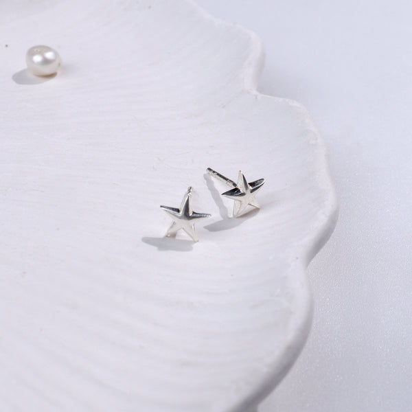 Silver starfish stud earrings on white textured surface