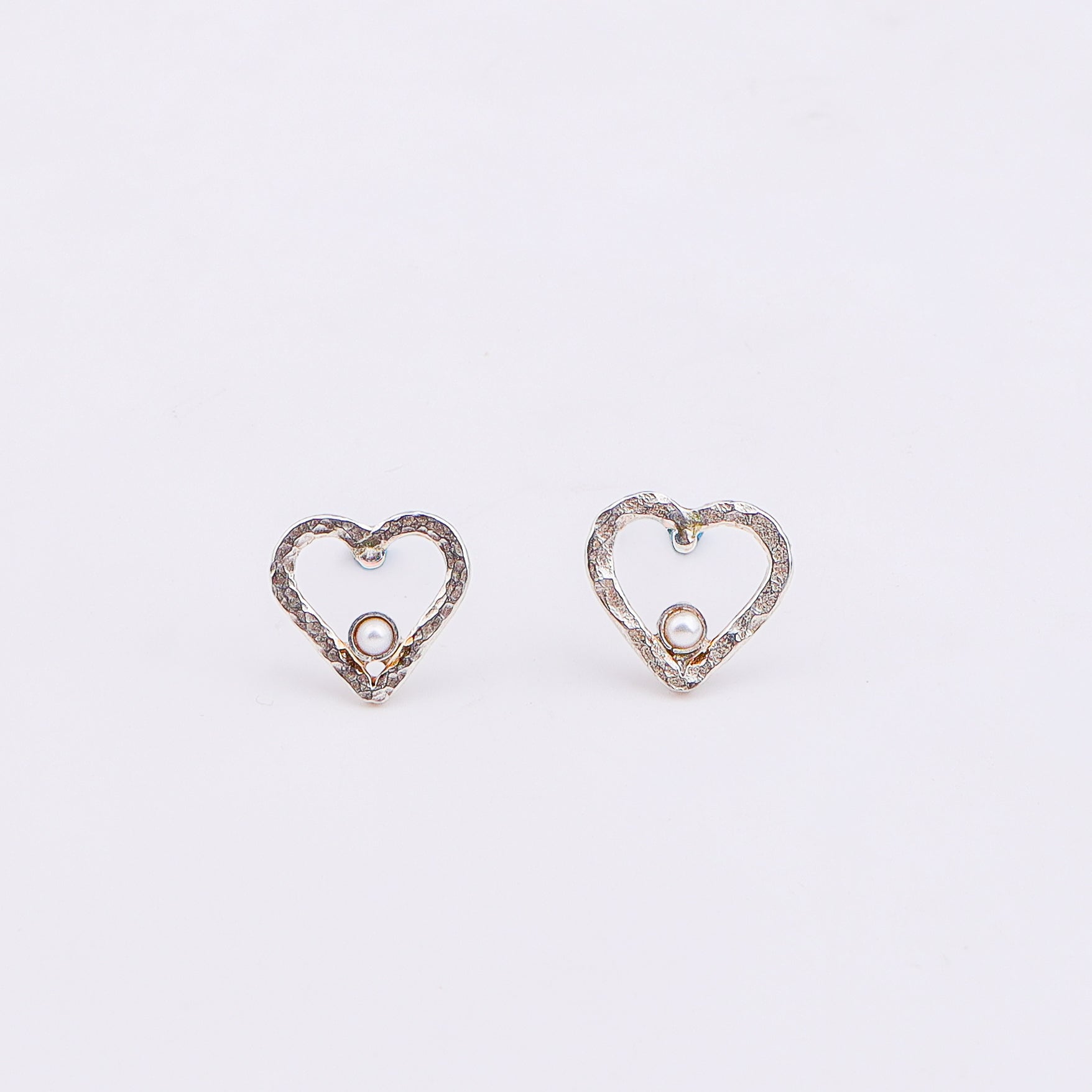 Close-up of silver heart pearl earrings on white background