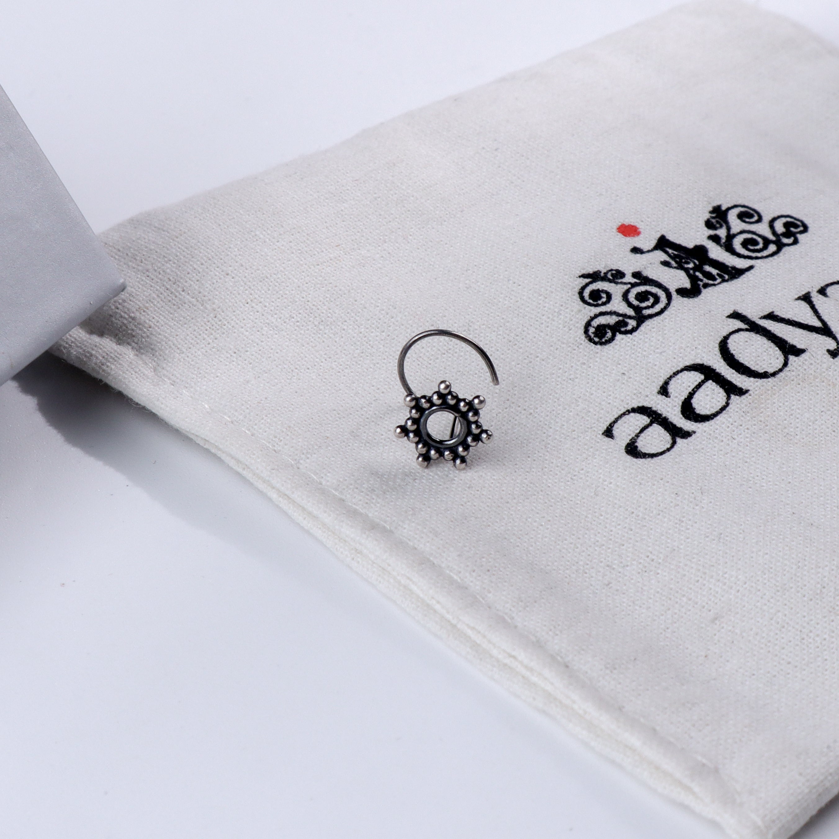 Minimal silver nose pin with circular design on Aadyaa jewelry pouch