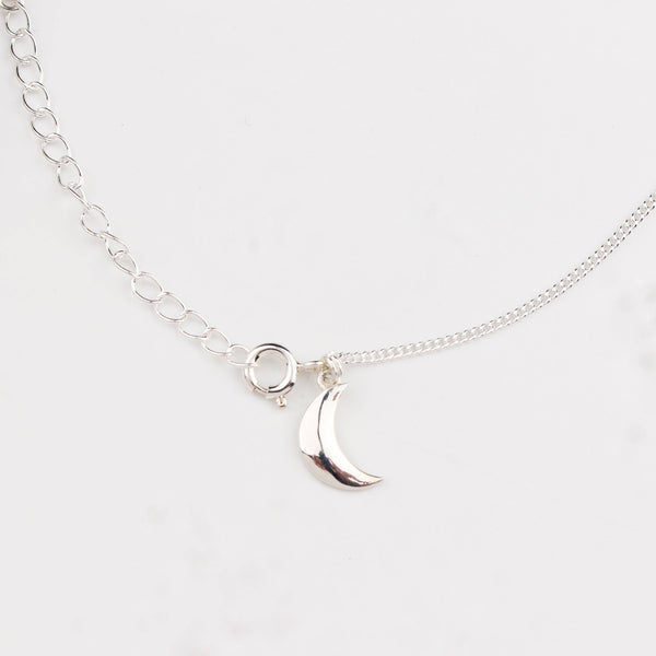 Close-up of silver crescent moon charm anklet detailing