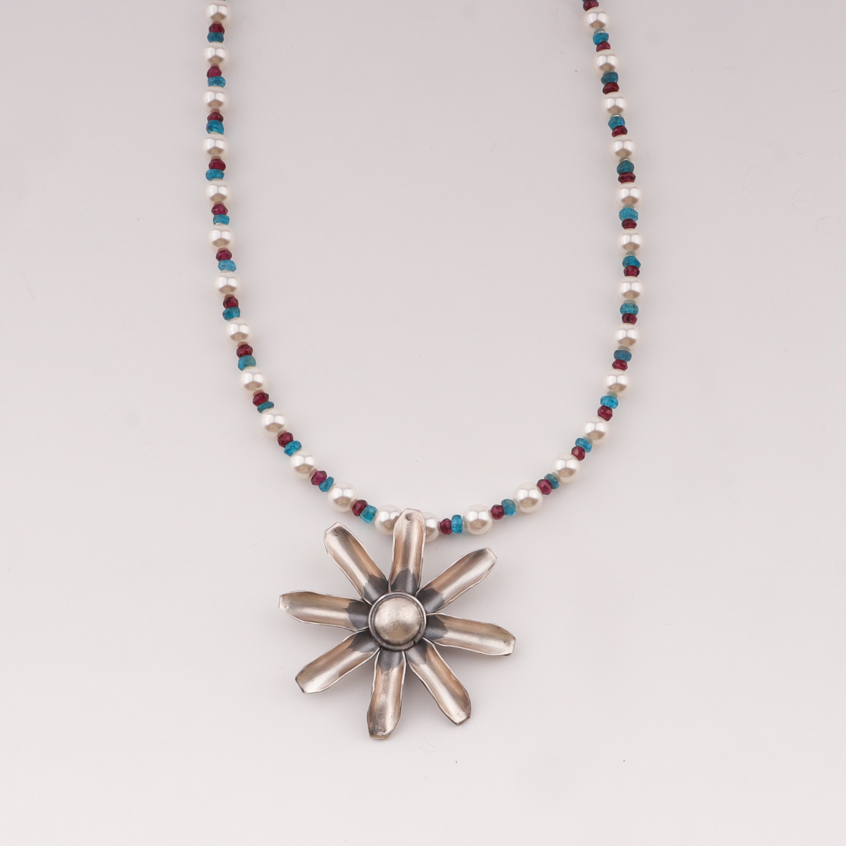 Close-up of beaded necklace with flower pendant, pearls, and stones