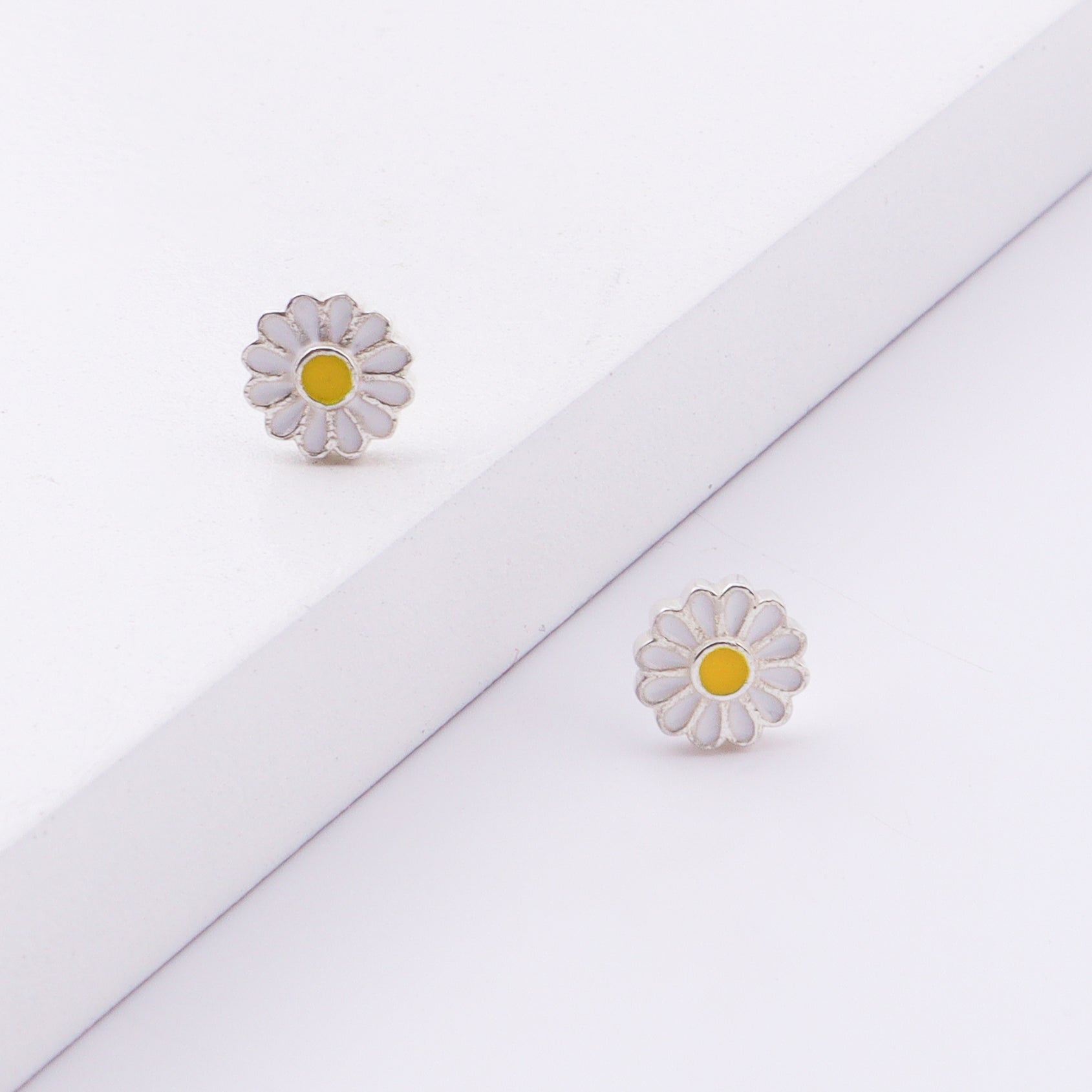 Close-up of daisy enamel stud earrings on white background