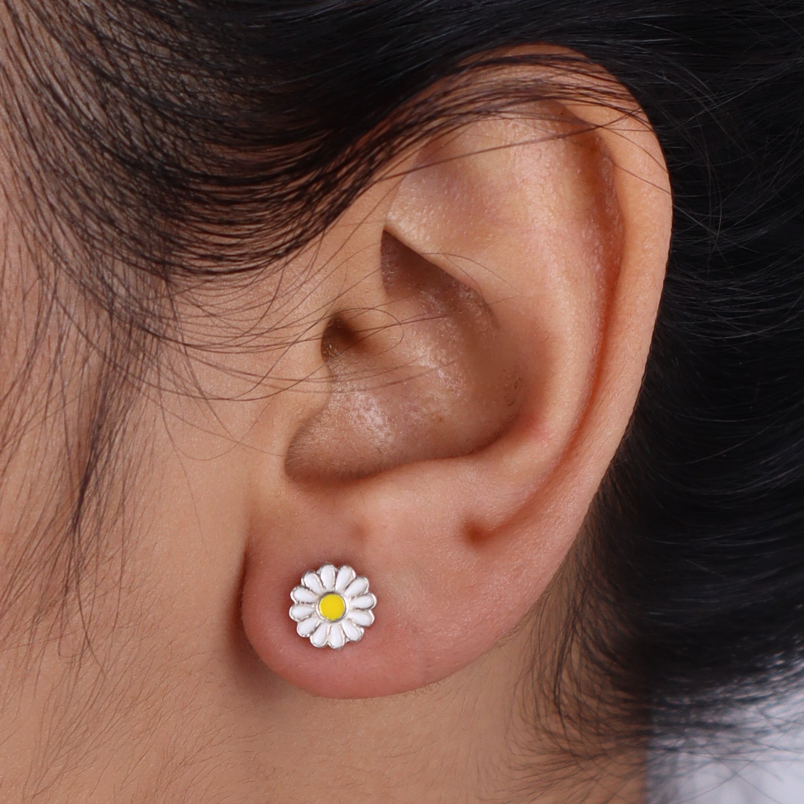 Model showing daisy enamel earrings on ear