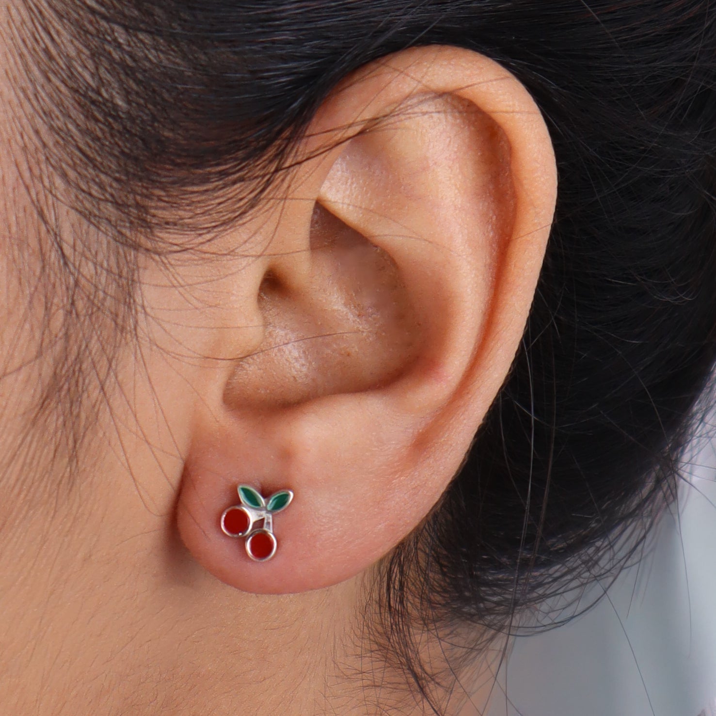 Model wearing cherry enamel earrings with black hair