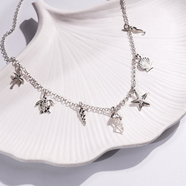 Silver Sea Charm Necklace with starfish, shell, and palm tree charms on white ceramic dish