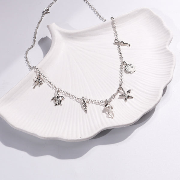 Silver sea charm necklace with starfish, shell, turtle, and palm tree charms on white shell dish