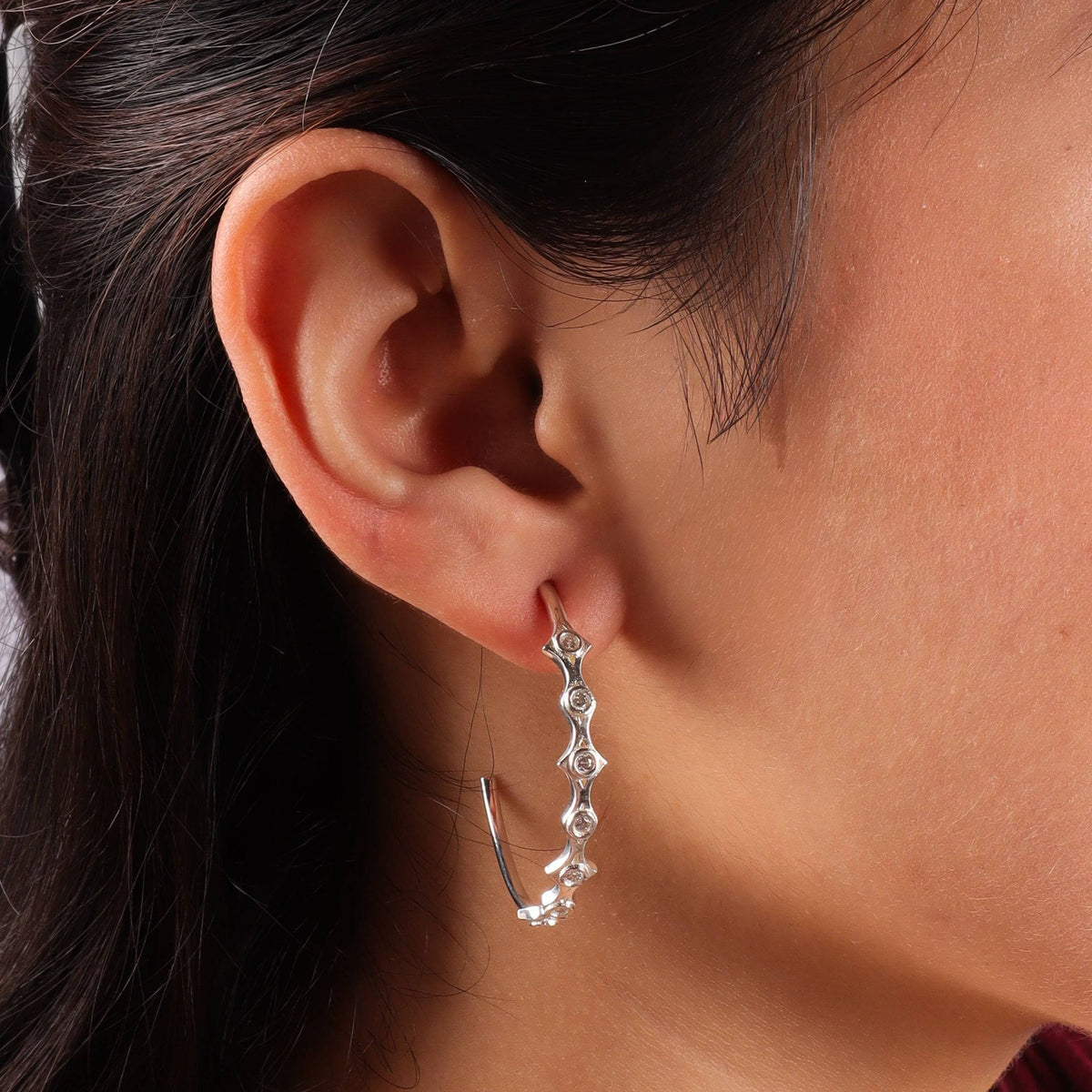Close-up of silver diamond-shaped hoop earrings with CZ stones worn by model